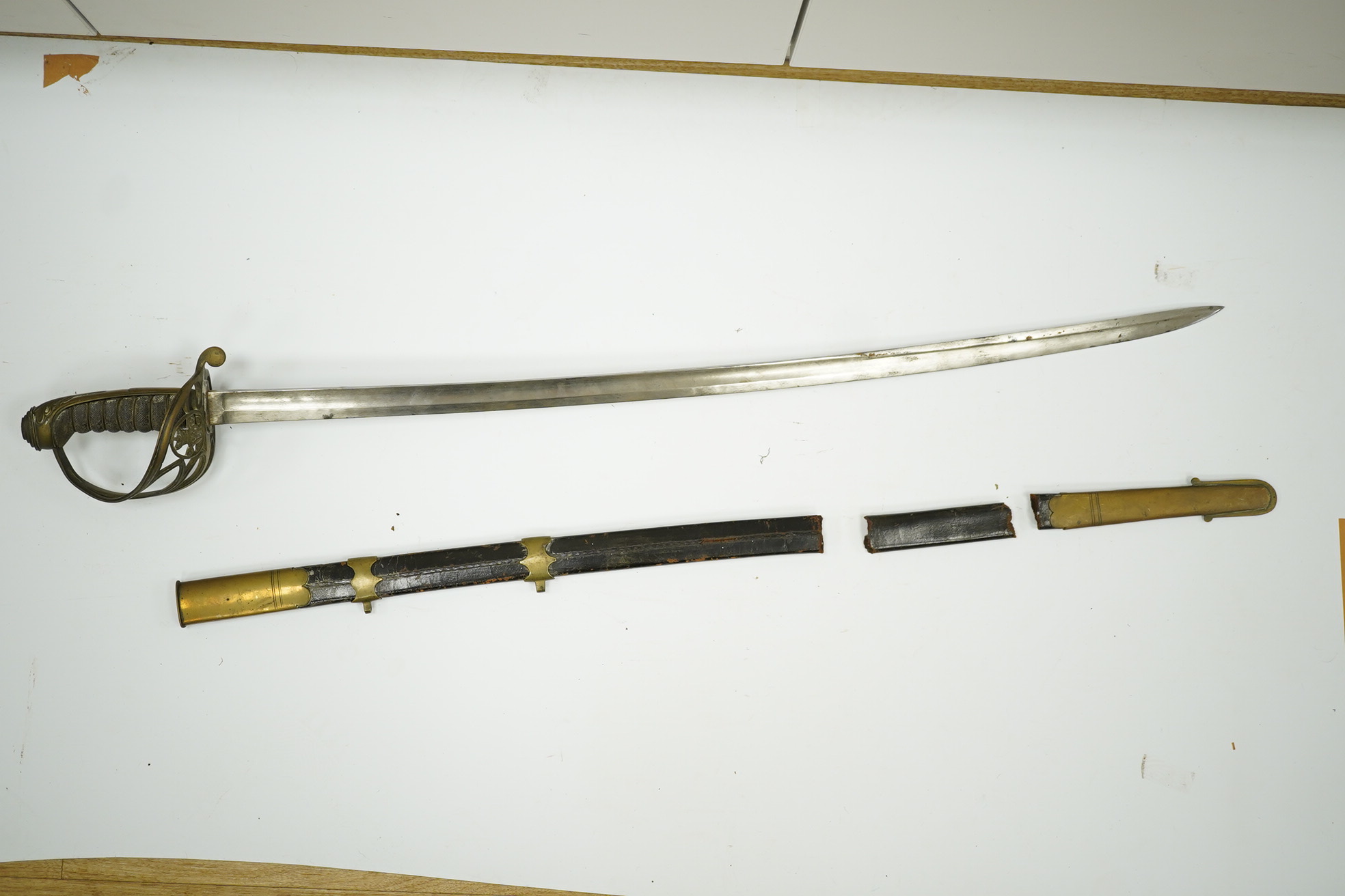 An 1845 pattern infantry officer’s sword, with plain slightly curved blade, regulation solid brass guard, and wire bound fish covered grip, in its brass mounted leather scabbard. Condition - poor to fair, blade cleaned b